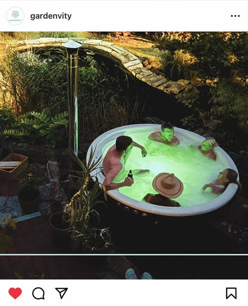 Group of friends enjoying an evening soak in a round hot tub with green LED lighting, surrounded by lush plants for ambient outdoor wellness.