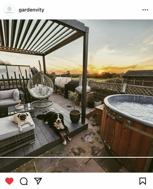 Sunset patio scene with a wooden hot tub, outdoor lounge furniture, and two dogs resting, highlighting a relaxing backyard retreat.