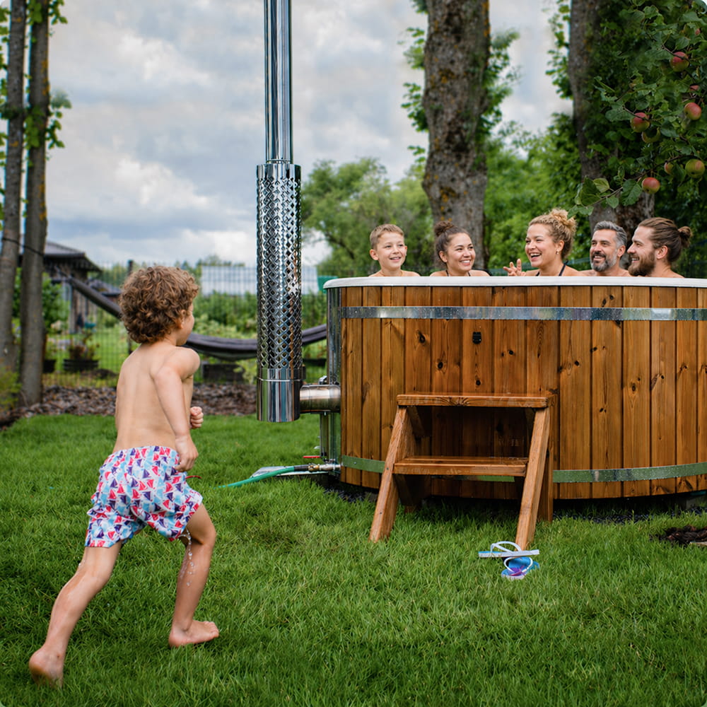Familie genießt einen Hot Tub im Garten, während ein Kind darauf zuläuft