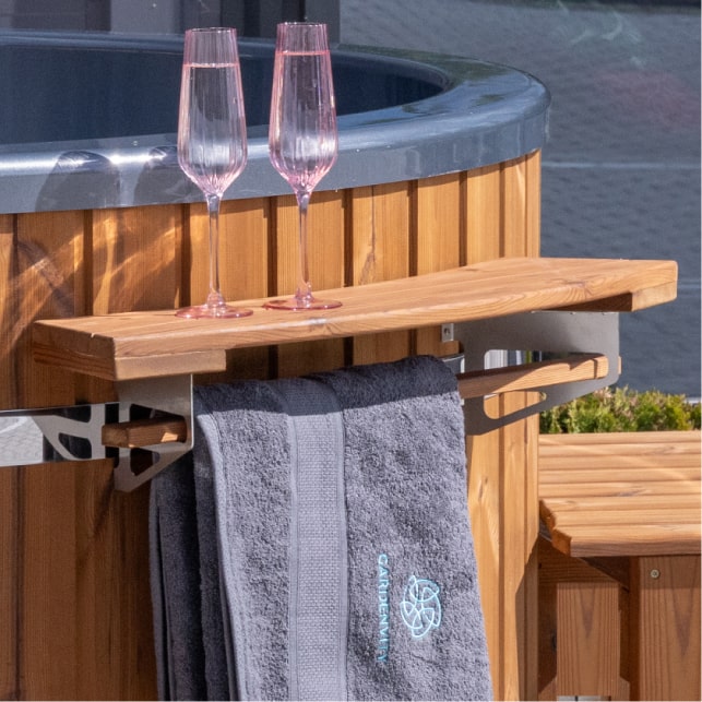 Nahaufnahme einer Holzablage am Hot Tub mit zwei rosafarbenen Champagnergläsern und einem grauen Handtuch darunter