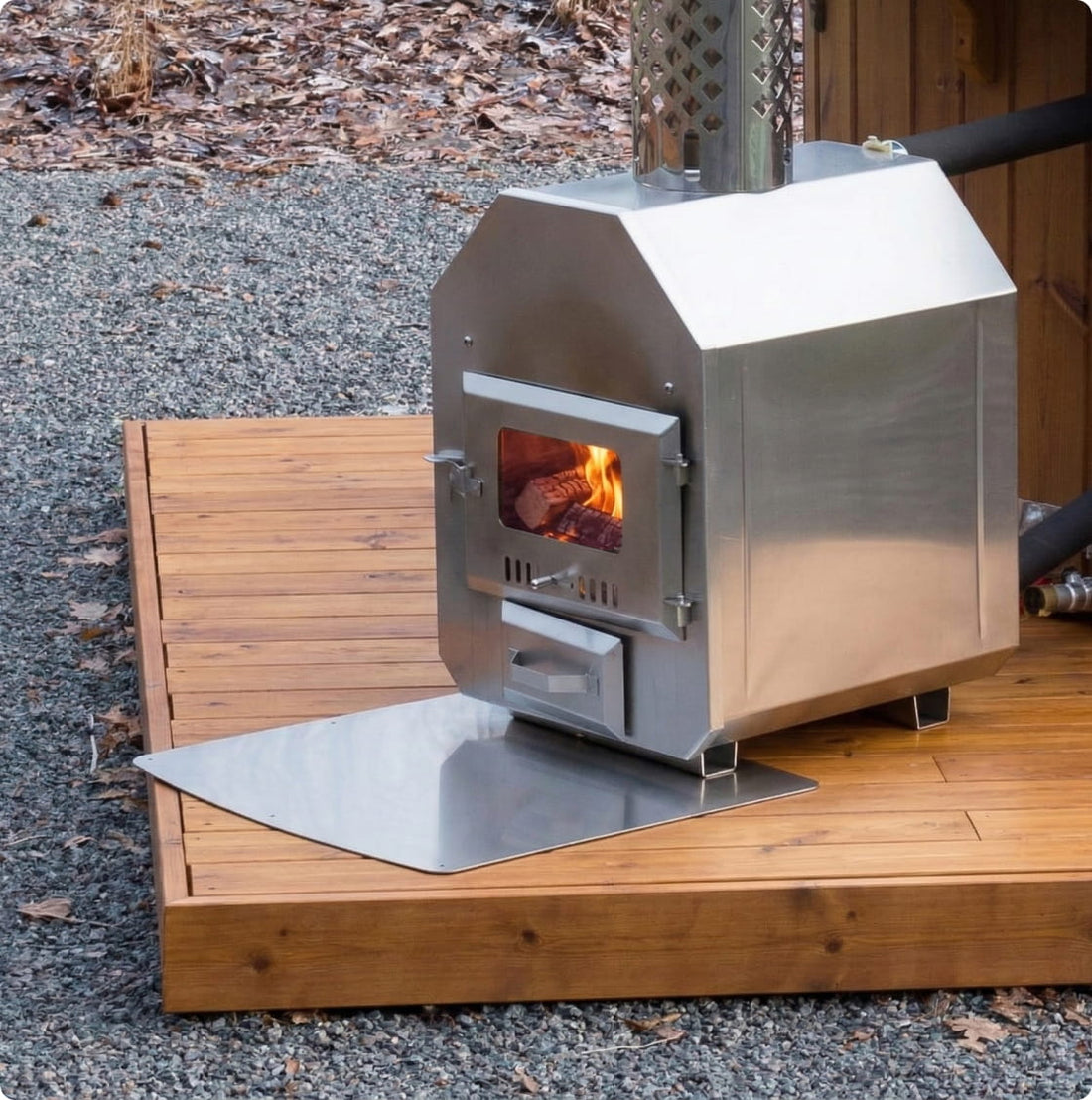 Außenliegender Holzofen aus Edelstahl auf einer Ascheplatte mit brennendem Feuer im Inneren.