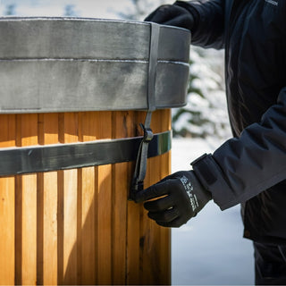 Close-up of person wearing black gloves securing strap on wooden hot tub cover outdoors in winter setting