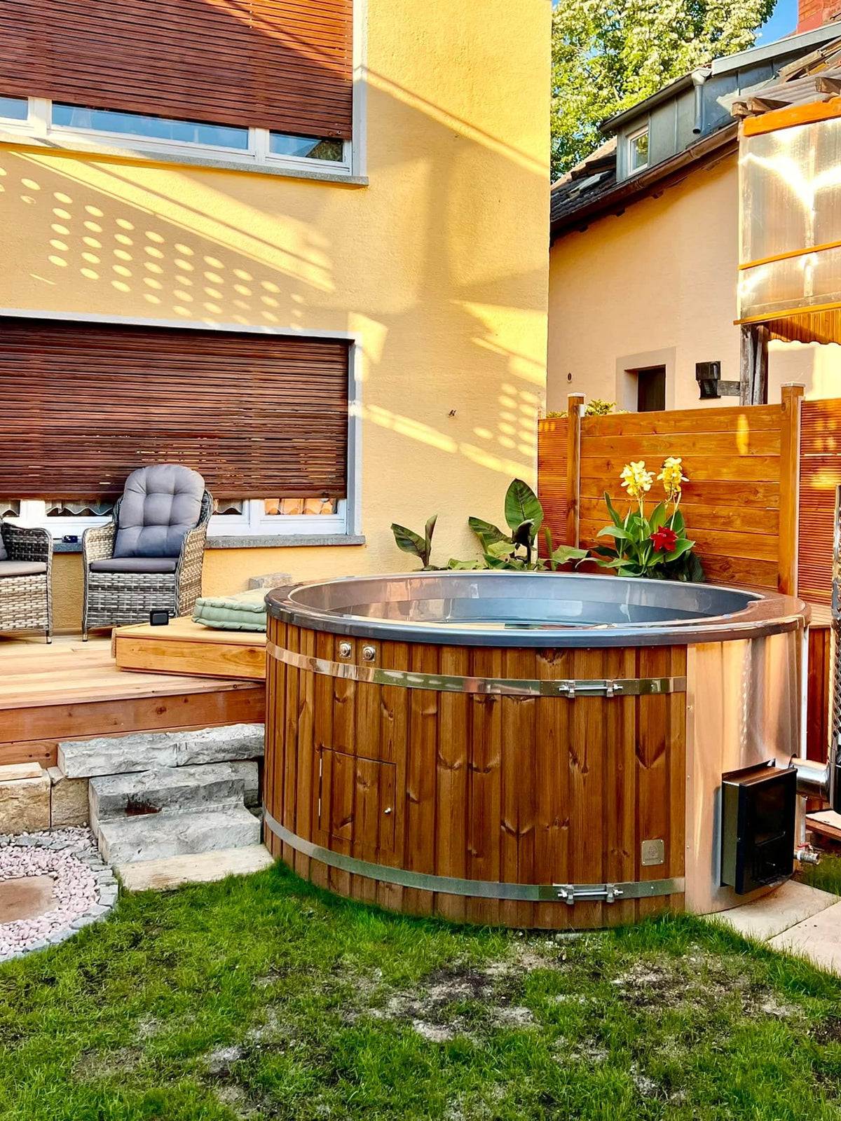 Gardenvity Holzofen-Whirlpool im Stadtgarten neben einem gelben Haus mit Terrassenmöbeln.