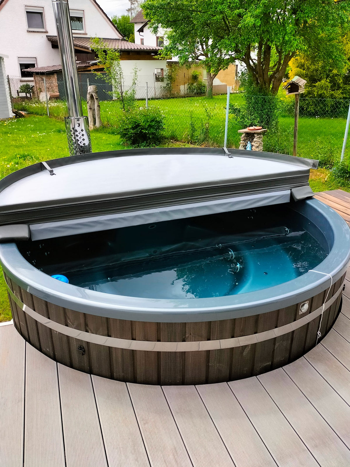 Kompakter Gardenvity Holzofen-hot tub mit isolierender Abdeckung in einem kleinen grünen Hinterhof.