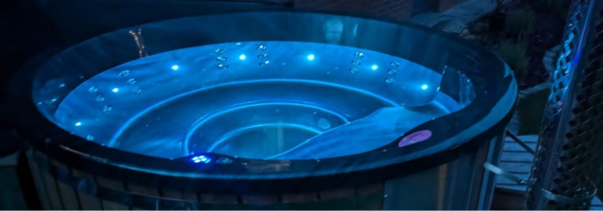 Nachtansicht eines runden hot tub, beleuchtet von blauen LED-Leuchten, mit sichtbaren Wasserstrahlen im Inneren