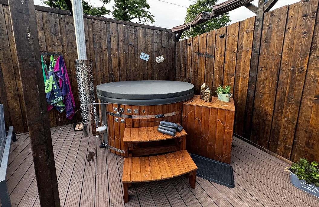 Auf der Terrasse befindet sich ein runder Hot Tub mit Abdeckung, Filterkasten, geschwungenen Stufen und einem Ofen mit Kamin.